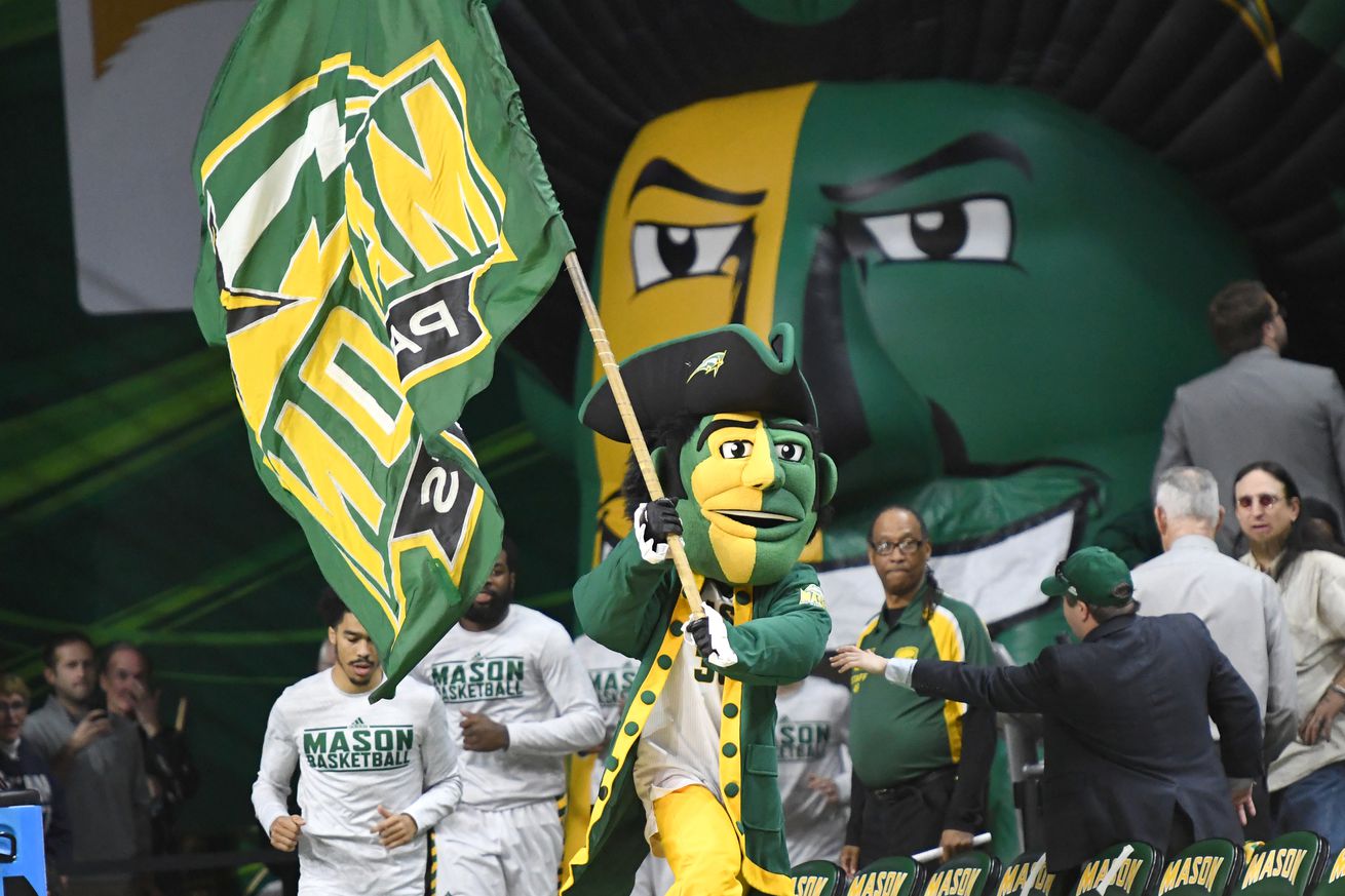 The George Mason mascot runs with a flag at a basketball game.