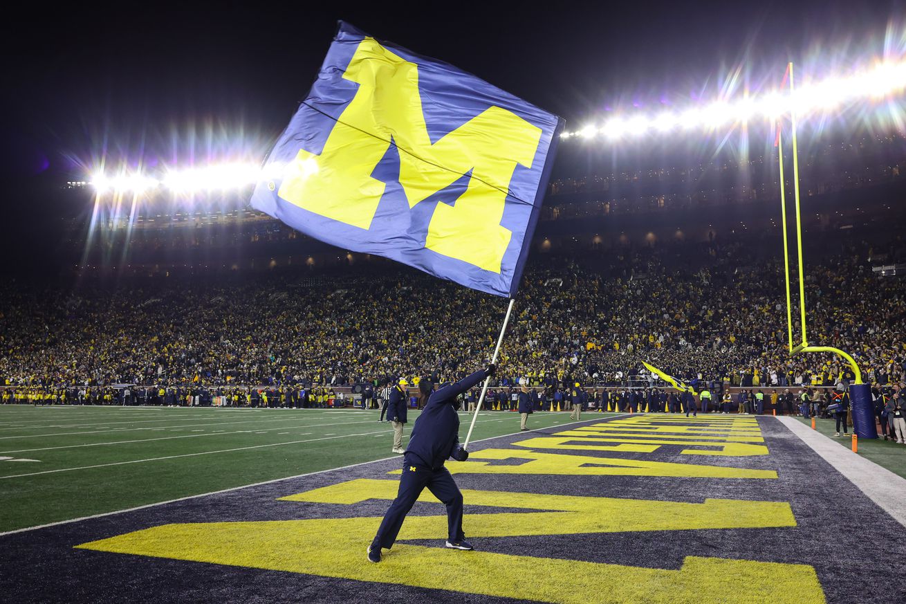 A Michigan cheerleader waves a giant flag with the Michigan block “M” logo after a touchdown during the fourth quarter of a regular season Big Ten Conference college football game between the Northwestern Wildcats and the Michigan Wolverines on November 23, 2024 at Michigan Stadium in Ann Arbor, Michigan.